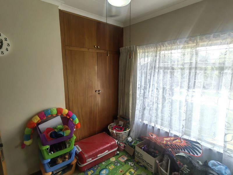 A bedroom featuring a built-in wooden wardrobe and a ceiling fan, with natural light entering through the window.