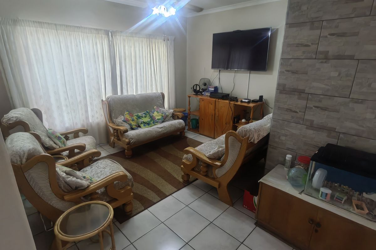 A comfortable living room featuring tiled flooring, a stone-clad feature wall, and a ceiling fan, offering a functional space for relaxation.