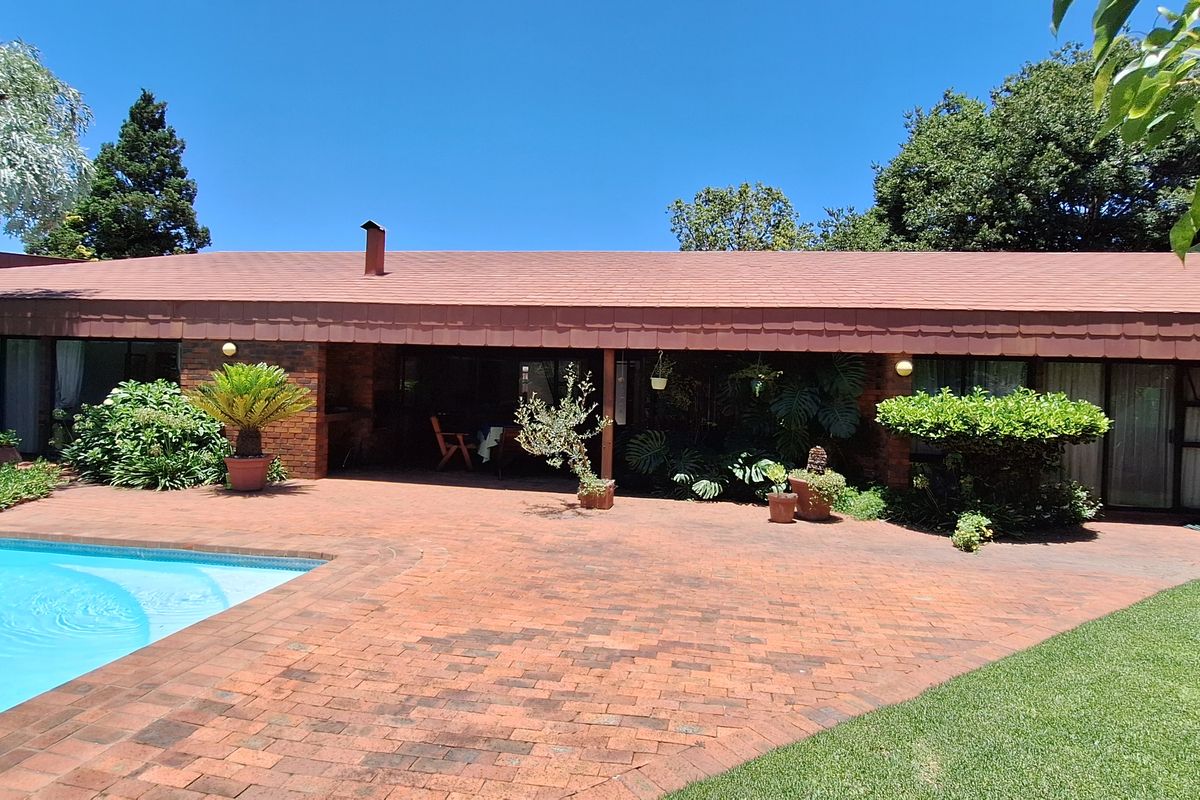 Rear view of the property featuring a brick-paved patio area, a swimming pool, and established garden landscaping.