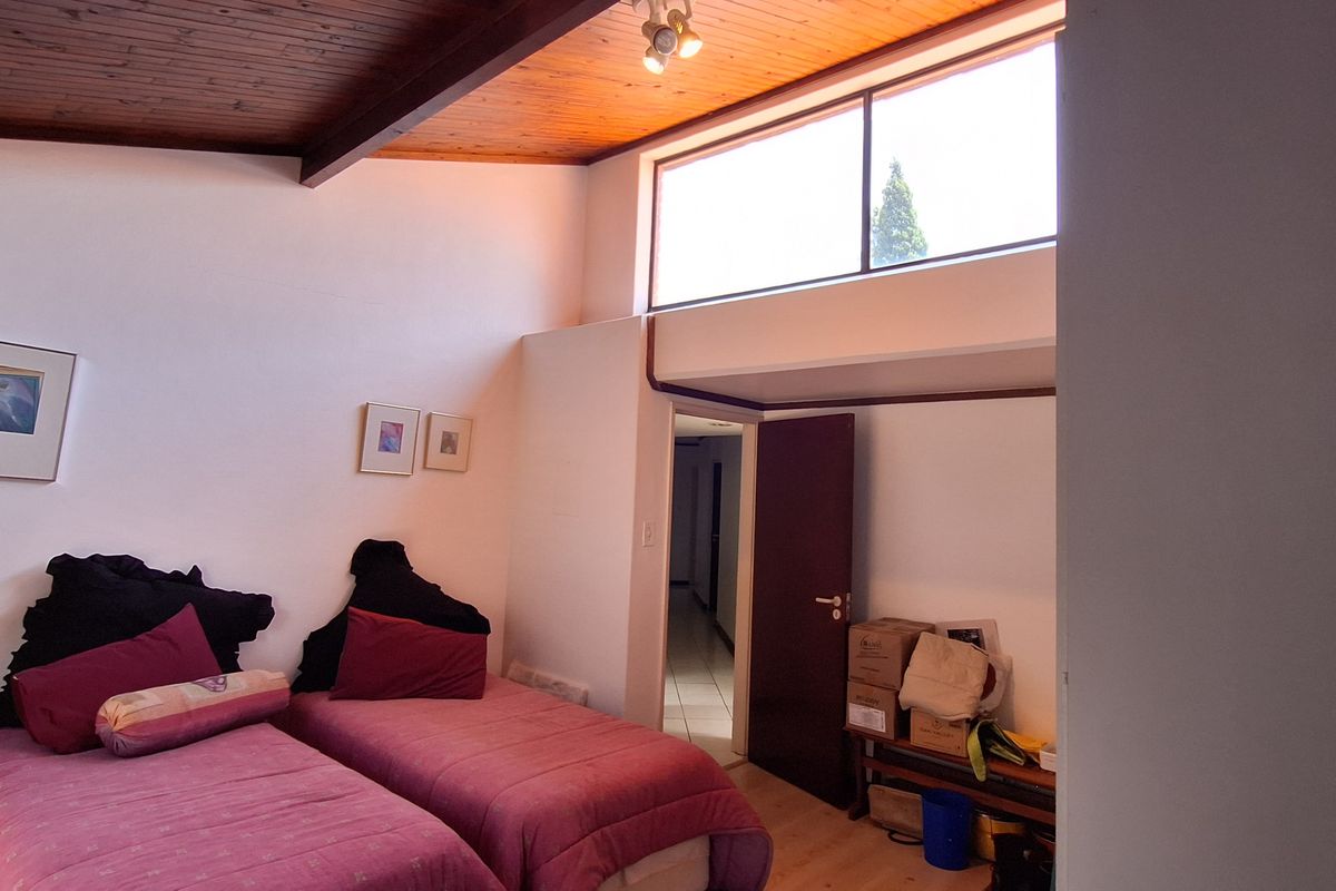 A bedroom featuring a high vaulted timber ceiling, clerestory windows for natural light, and direct access to an internal hallway.