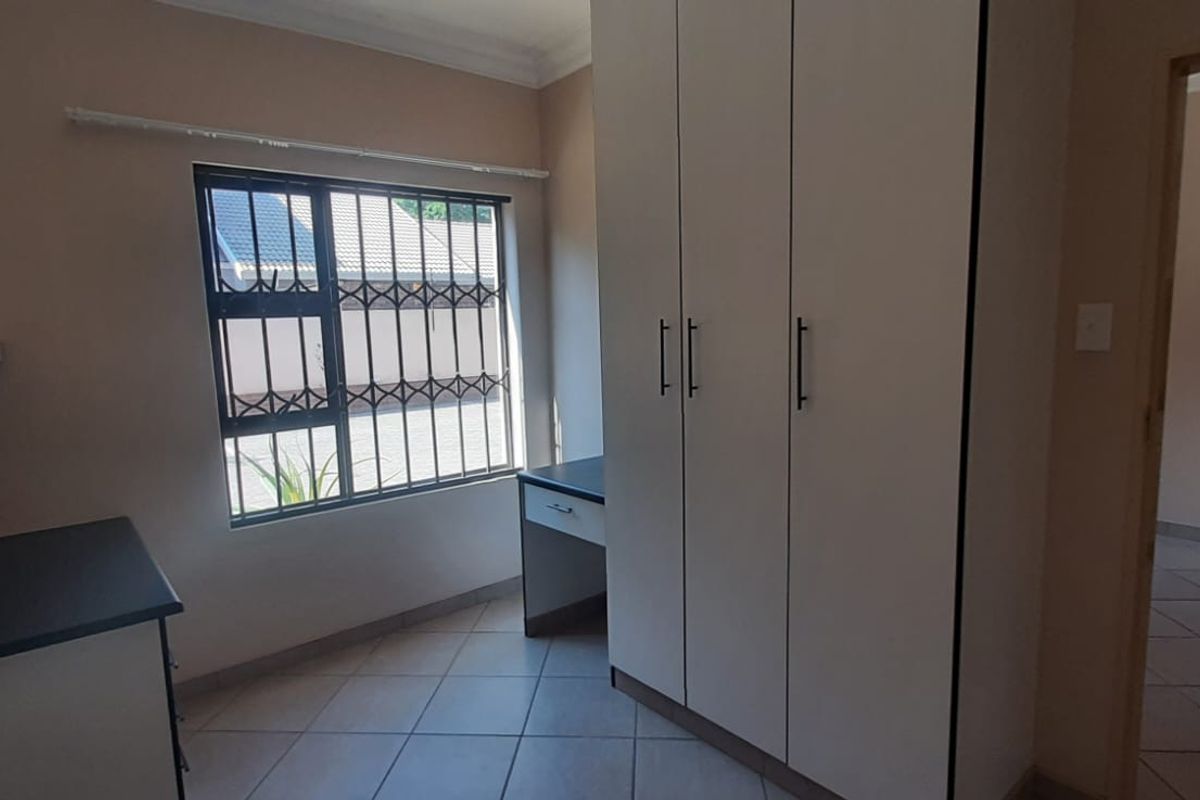 A bedroom featuring built-in cupboards, a built-in desk, tiled flooring, and security bars on the window.