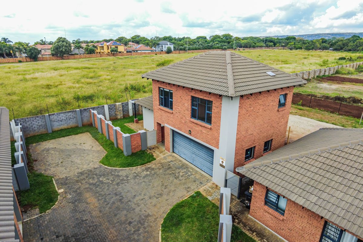 Aerial view of a double-story facebrick townhouse featuring a tiled roof, paved driveway, and secure perimeter walling in a residential estate setting.