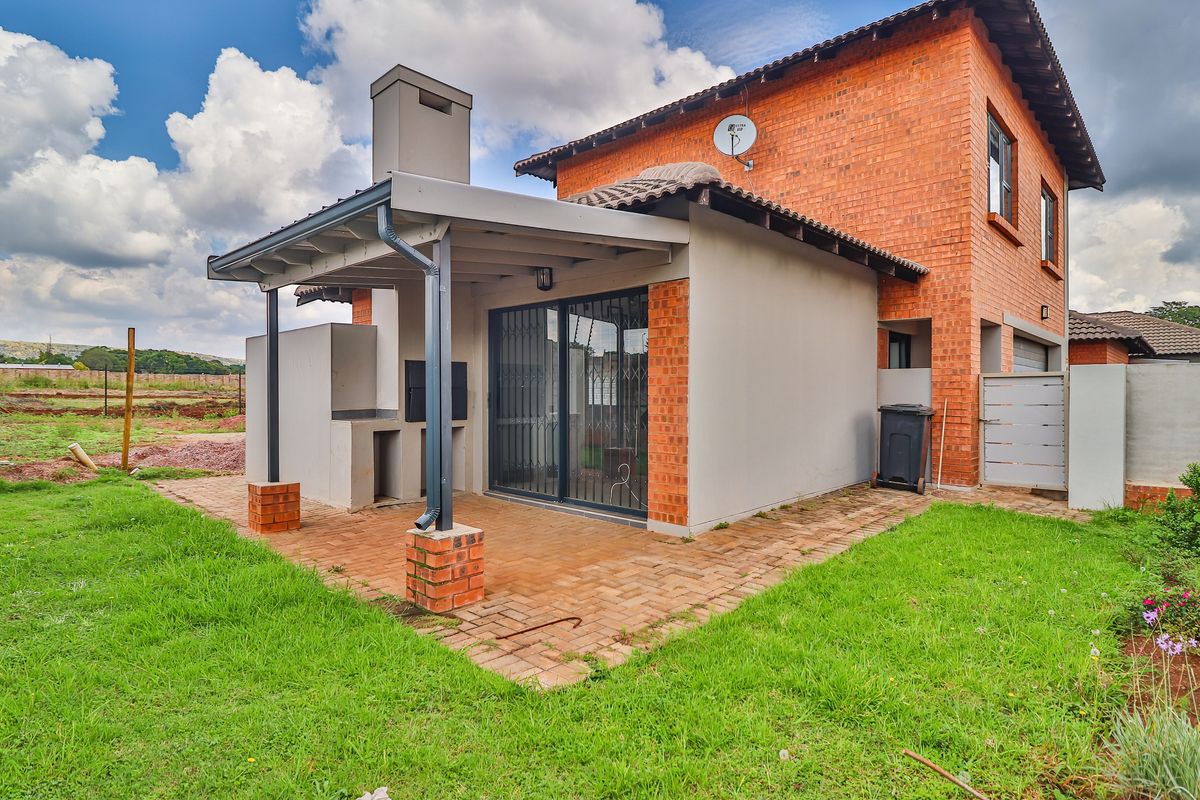 Rear view of the townhouse featuring a covered patio with a built-in braai, brick paving, and access to the garden through sliding doors.