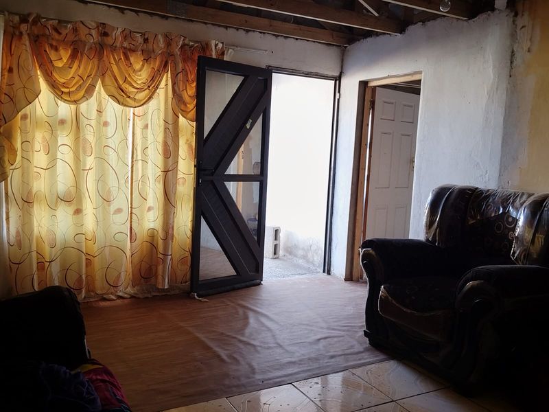 Living room area featuring exposed timber ceiling beams, tiled flooring, and direct access to an exterior space through a security gate.