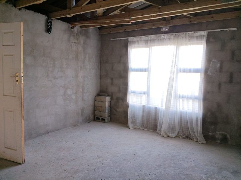 An unfinished bedroom space featuring exposed timber roof trusses, raw concrete block walls, and a concrete floor, offering a blank canvas for renovation.