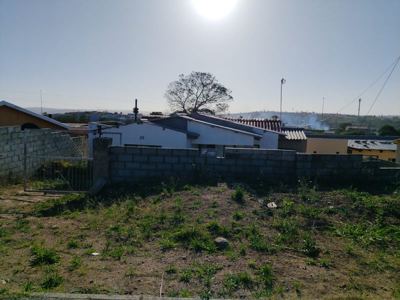 Rear view of the property showing an unpaved yard, concrete block boundary wall, and metal gate access.