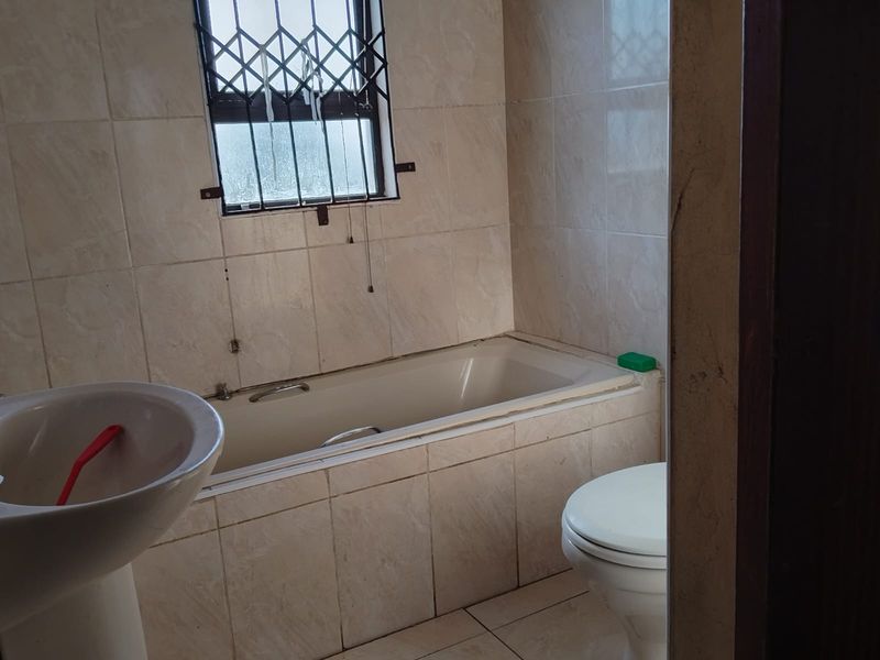 A functional bathroom featuring a built-in bathtub, pedestal basin, and toilet, finished with neutral wall and floor tiles.