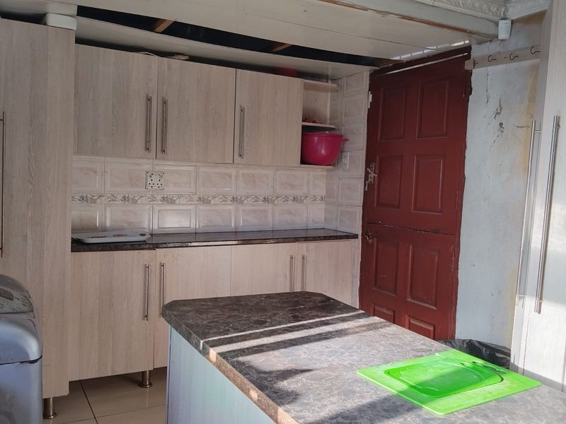 A kitchen area featuring light wood-finish cabinetry, tiled backsplash, and a central island, currently requiring ceiling and wall repairs.