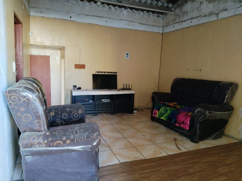 A living room area featuring ceramic floor tiles and an unfinished ceiling, requiring cosmetic updates and repairs to improve the overall condition.