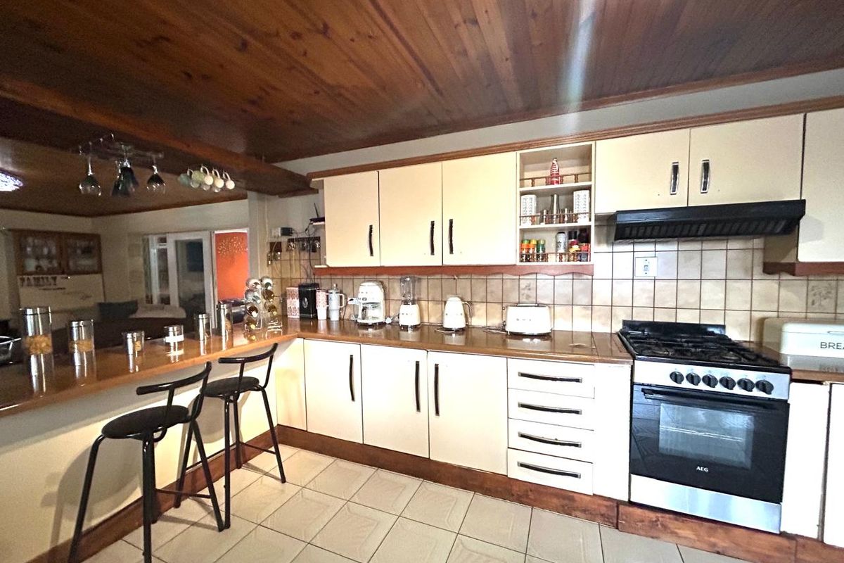 A functional kitchen featuring built-in cabinetry, a breakfast bar, tiled flooring, and a timber ceiling, offering a classic layout with integrated cooking appliances.