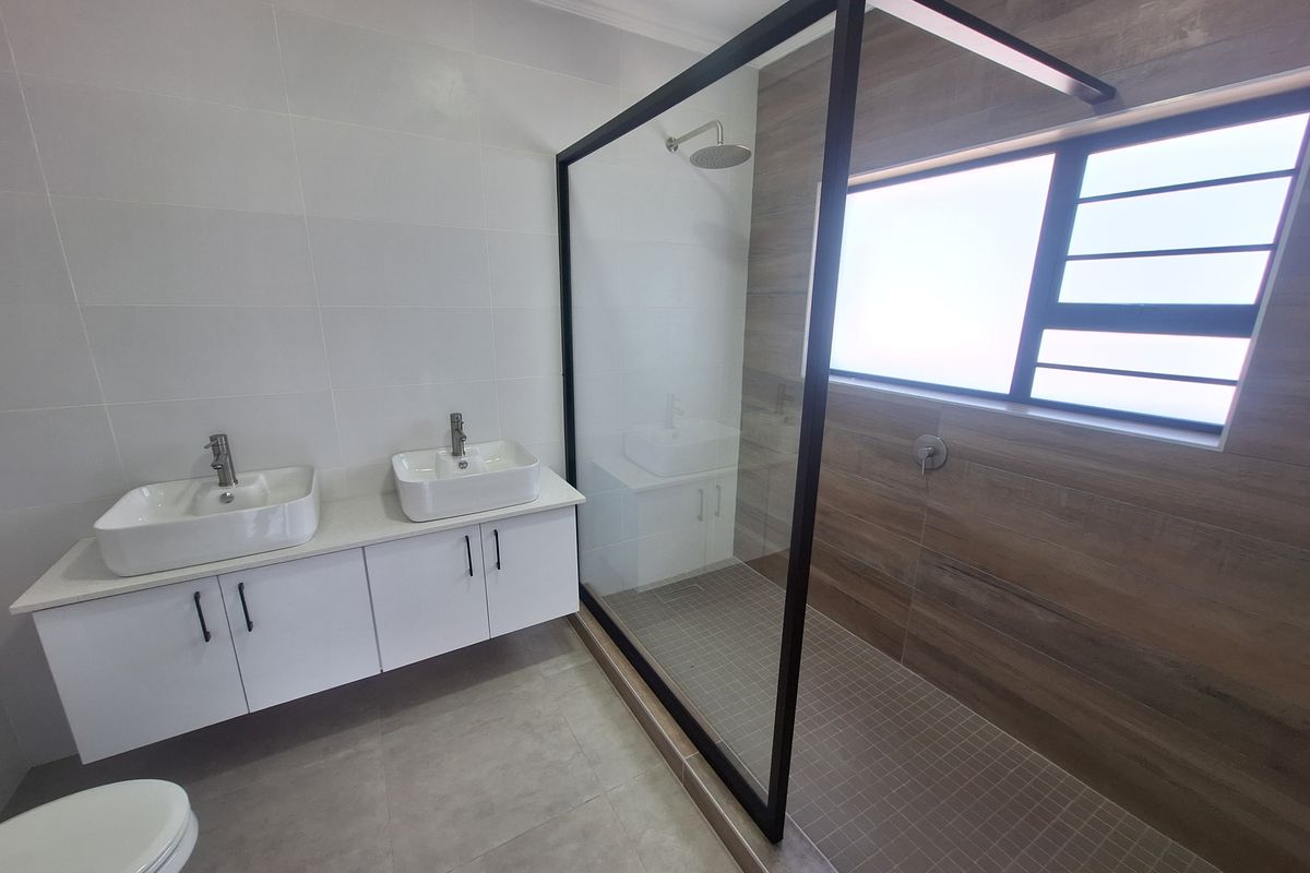 Modern bathroom featuring a double vanity with vessel sinks and a spacious walk-in shower with a sleek black frame and rain shower head.
