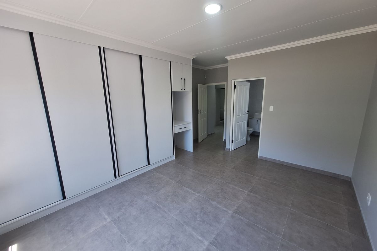 Spacious bedroom featuring modern grey floor tiles, extensive built-in wardrobe storage with an integrated vanity, and direct access to an en-suite bathroom.