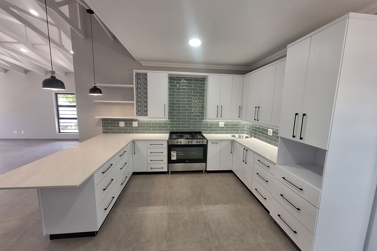 Modern kitchen featuring white cabinetry, stone countertops, subway tile backsplash, gas stove, and open-plan layout with exposed rafters.