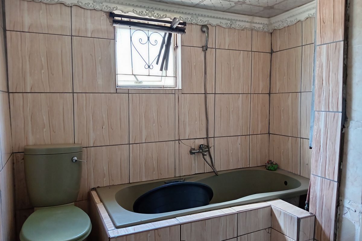A dated bathroom featuring a built-in bathtub, toilet, and wood-look wall tiles. The space requires renovation to update the fixtures and finishes.