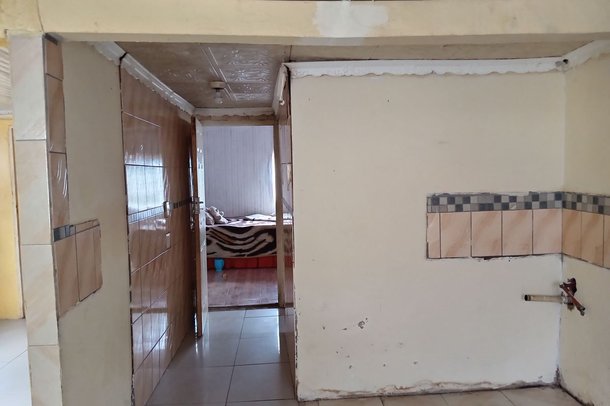 An unfinished kitchen area featuring tiled walls and flooring, requiring completion of wall finishes and plumbing fixtures to become a functional space.