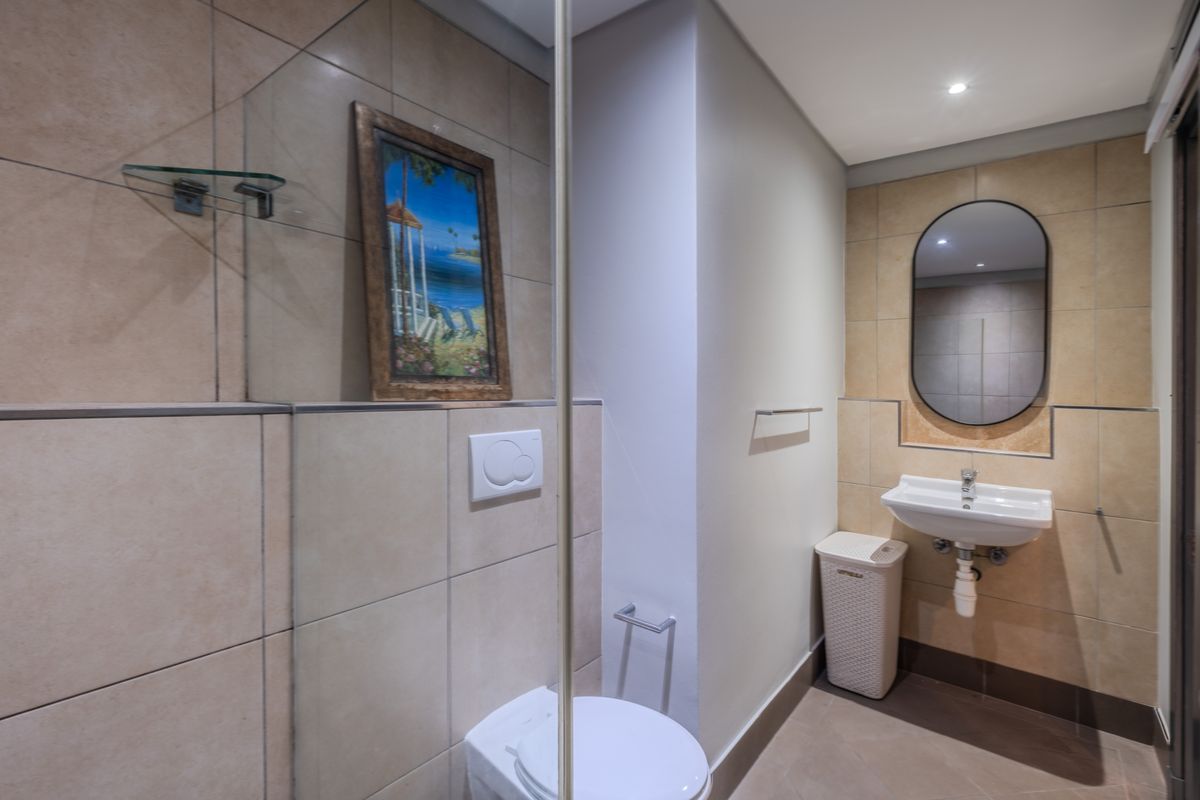 Modern bathroom featuring a wall-mounted toilet with concealed cistern, ceramic basin with chrome mixer, and tiled finishes with a glass shower screen.