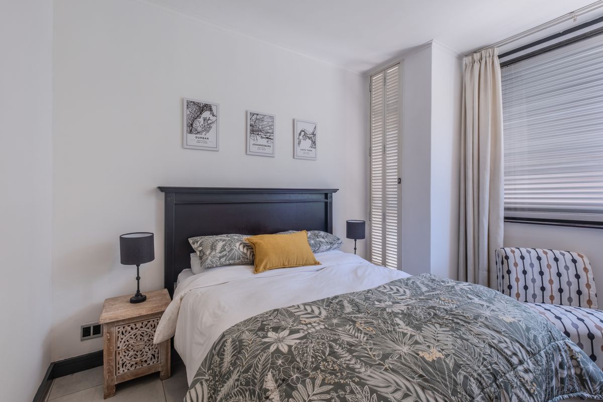 A well-maintained bedroom featuring tiled flooring, louvered shutters, and neutral wall finishes, providing a comfortable and bright living space.