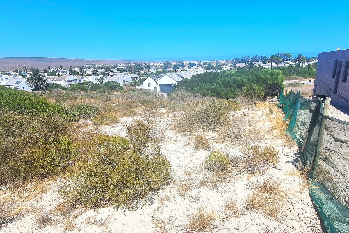 A view of the vacant residential land showing sandy terrain, perimeter fencing, and the adjacent building structure under construction.