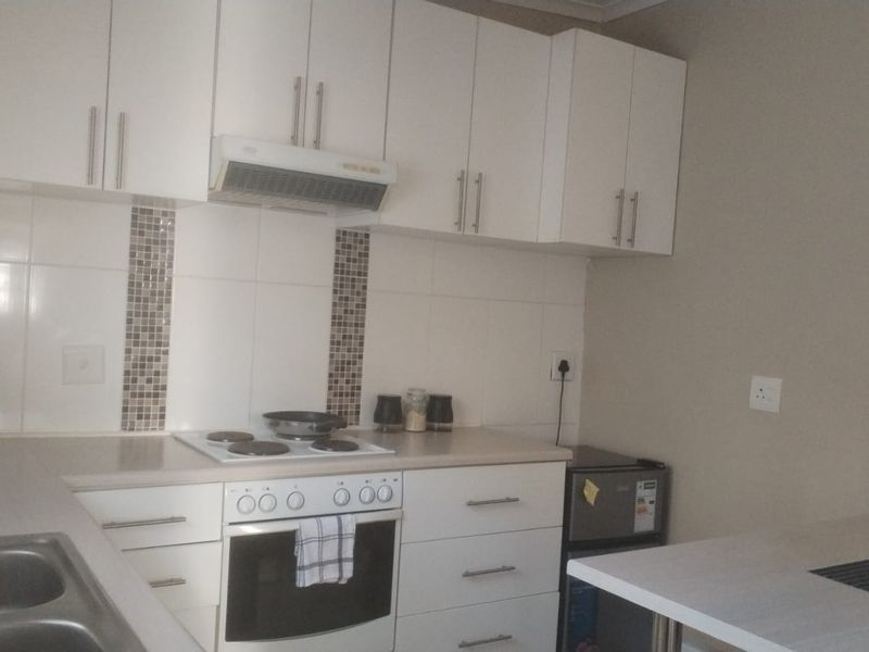 A functional kitchen featuring white cabinetry, laminate countertops, a tiled backsplash, and integrated cooking appliances including an oven and hob.