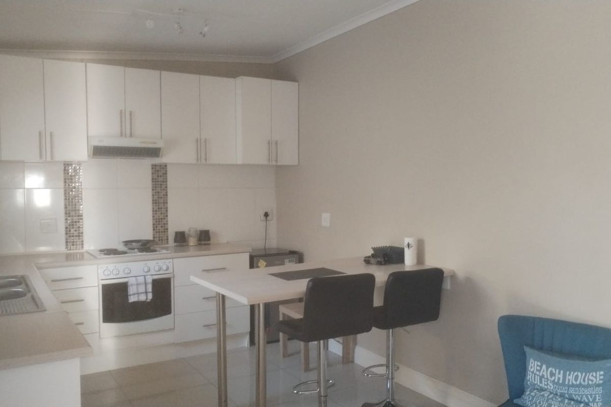 A functional kitchen featuring white cabinetry, integrated appliances, a tiled splashback, and a convenient breakfast bar area.
