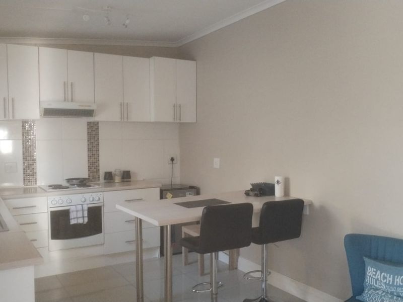 A functional kitchen featuring white cabinetry, integrated appliances, a tiled splashback, and a convenient breakfast bar area.