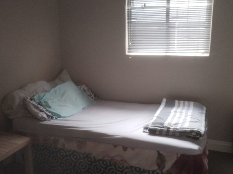A simple bedroom featuring neutral walls and a window fitted with venetian blinds.
