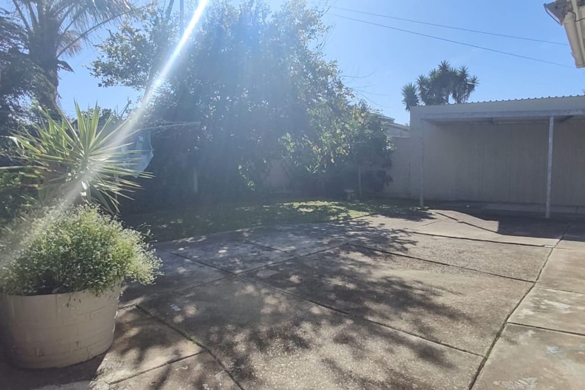 Rear exterior area featuring a concrete paved patio, a covered carport structure, and a private garden space.