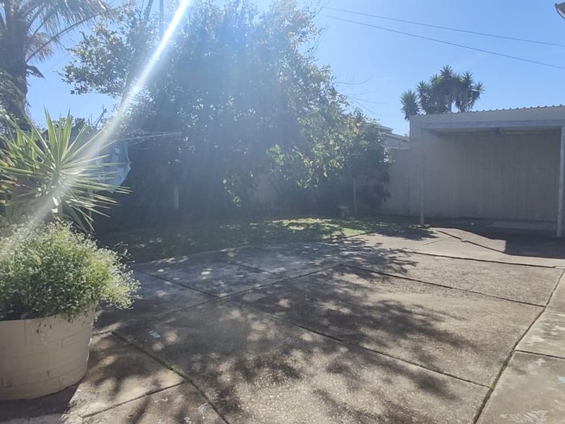 Rear exterior area featuring a concrete paved patio, a covered carport structure, and a private garden space.