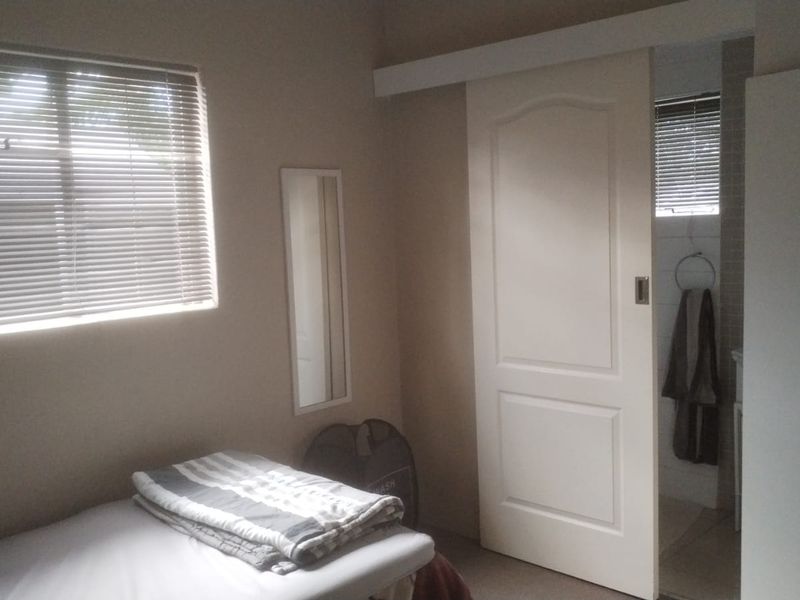 A bedroom featuring a sliding door leading to an en-suite bathroom, equipped with venetian blinds and a wall-mounted mirror.