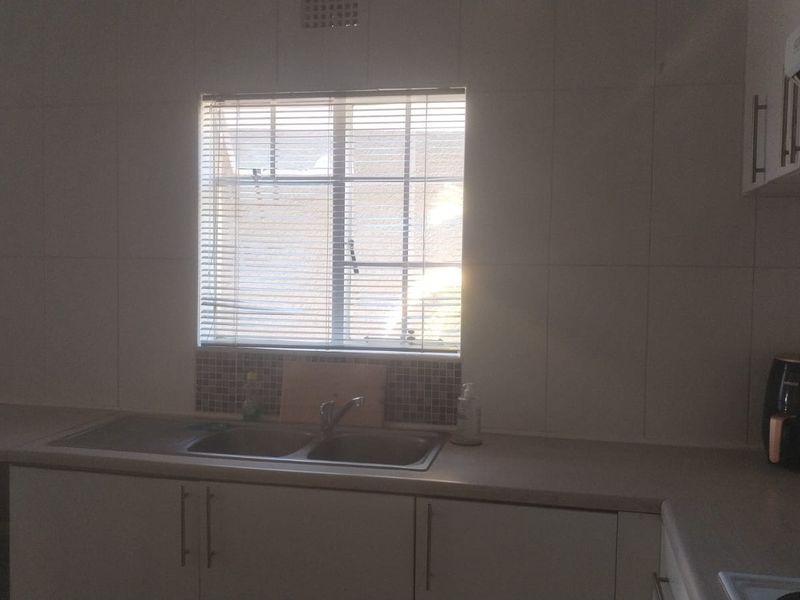 A functional kitchen area featuring built-in cabinetry, a double bowl stainless steel sink, tiled splashbacks, and an integrated extractor fan.