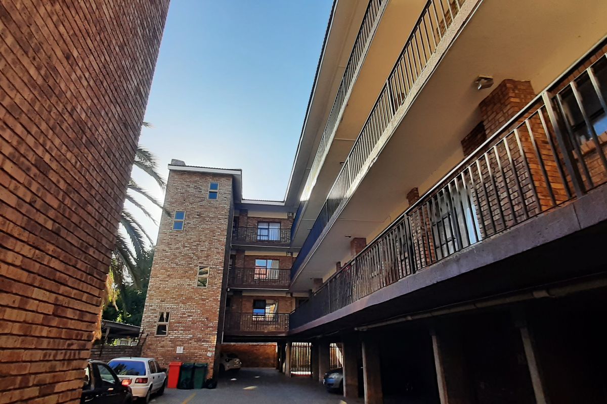Exterior view of a multi-story brick apartment building featuring open-air balconies and a ground-level covered parking area.