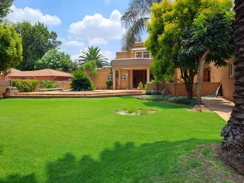 Spacious rear garden featuring a well-maintained lawn, swimming pool, and paved patio area adjacent to the brick-built house.
