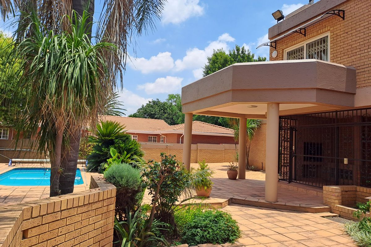Rear exterior view featuring a covered patio area, brick paving, and a swimming pool set within a landscaped garden.