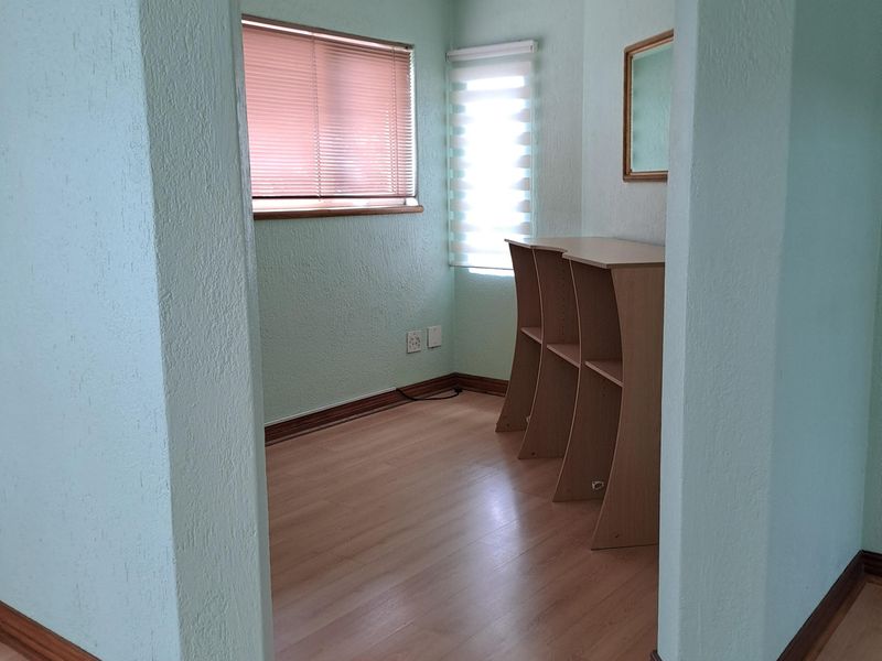 A compact office space featuring laminate flooring, dual window treatments, and neutral wall finishes, providing a functional area for work or study.