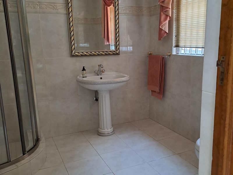 A functional bathroom featuring a pedestal basin, a corner shower enclosure, and neutral wall and floor tiling.