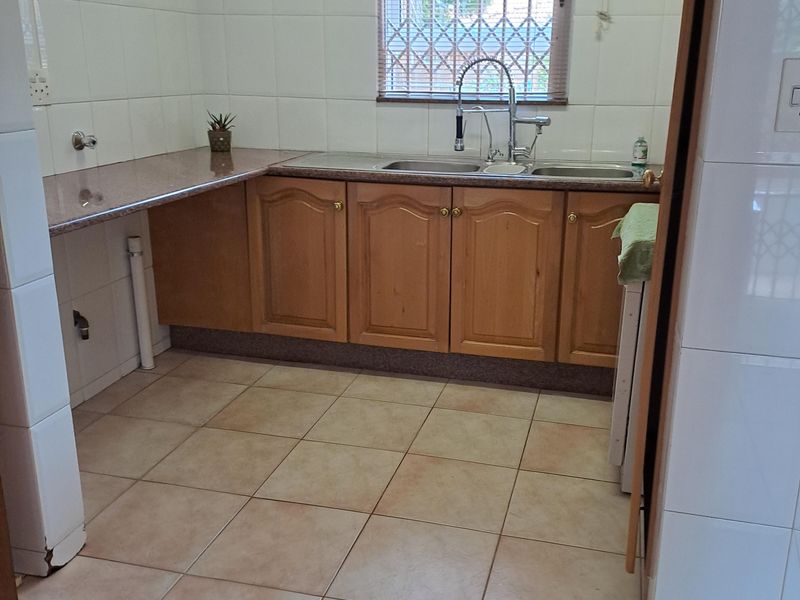 A functional kitchen featuring wooden cabinetry, granite countertops, a double sink, and tiled finishes, offering a clean space ready for modernization.