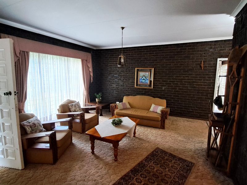 A living room featuring dark exposed brick walls, carpeted flooring, and a large window with natural light.