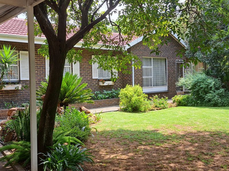 A well-maintained rear garden featuring a brick facade house, a covered patio area, and established landscaping with a paved walkway.