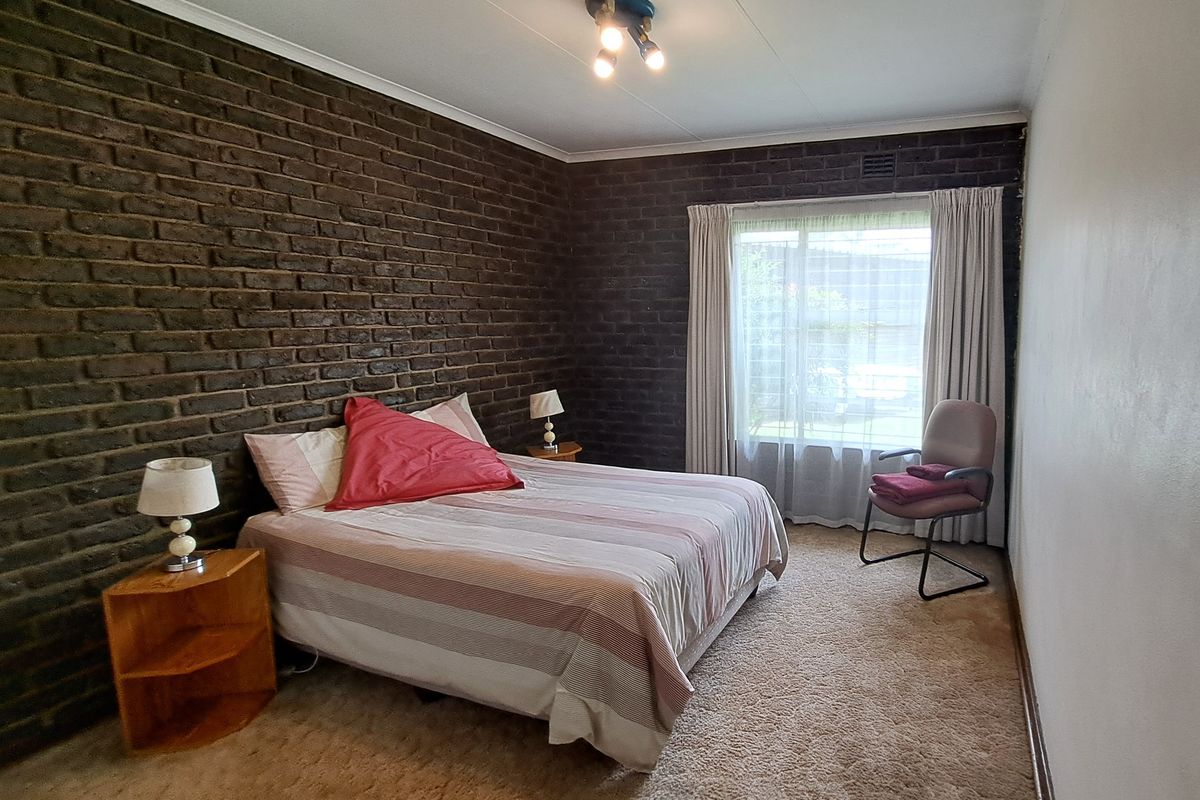A bedroom featuring a prominent dark exposed brick feature wall, carpeted flooring, and natural light through a window with curtain tracks.