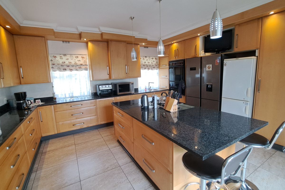 Spacious kitchen featuring light wood cabinetry, dark granite countertops, a central island with breakfast bar seating, and integrated appliances.