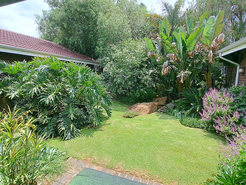 A lush, well-established private garden featuring a manicured lawn, mature shrubs, and brick-paved borders adjacent to the home's exterior.