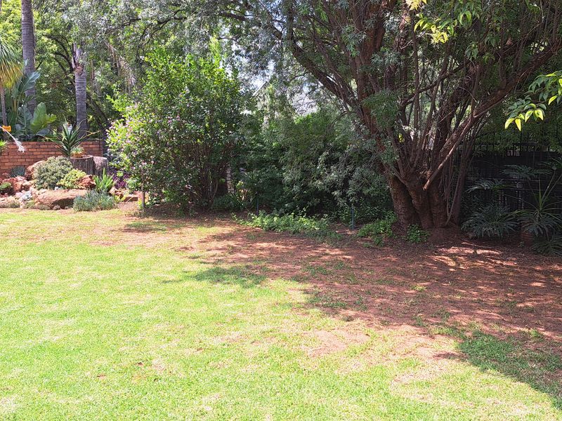 A well-established garden featuring a lush lawn, mature trees, and a brick retaining wall with landscaped garden beds.