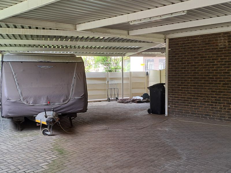 A spacious covered carport or garage area featuring paved flooring, brick walls, and a corrugated metal roof structure.