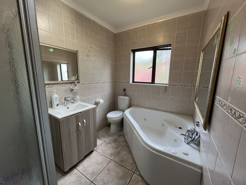 A functional bathroom featuring a corner spa bath, separate shower enclosure, vanity cabinet with basin, and neutral wall and floor tiling.