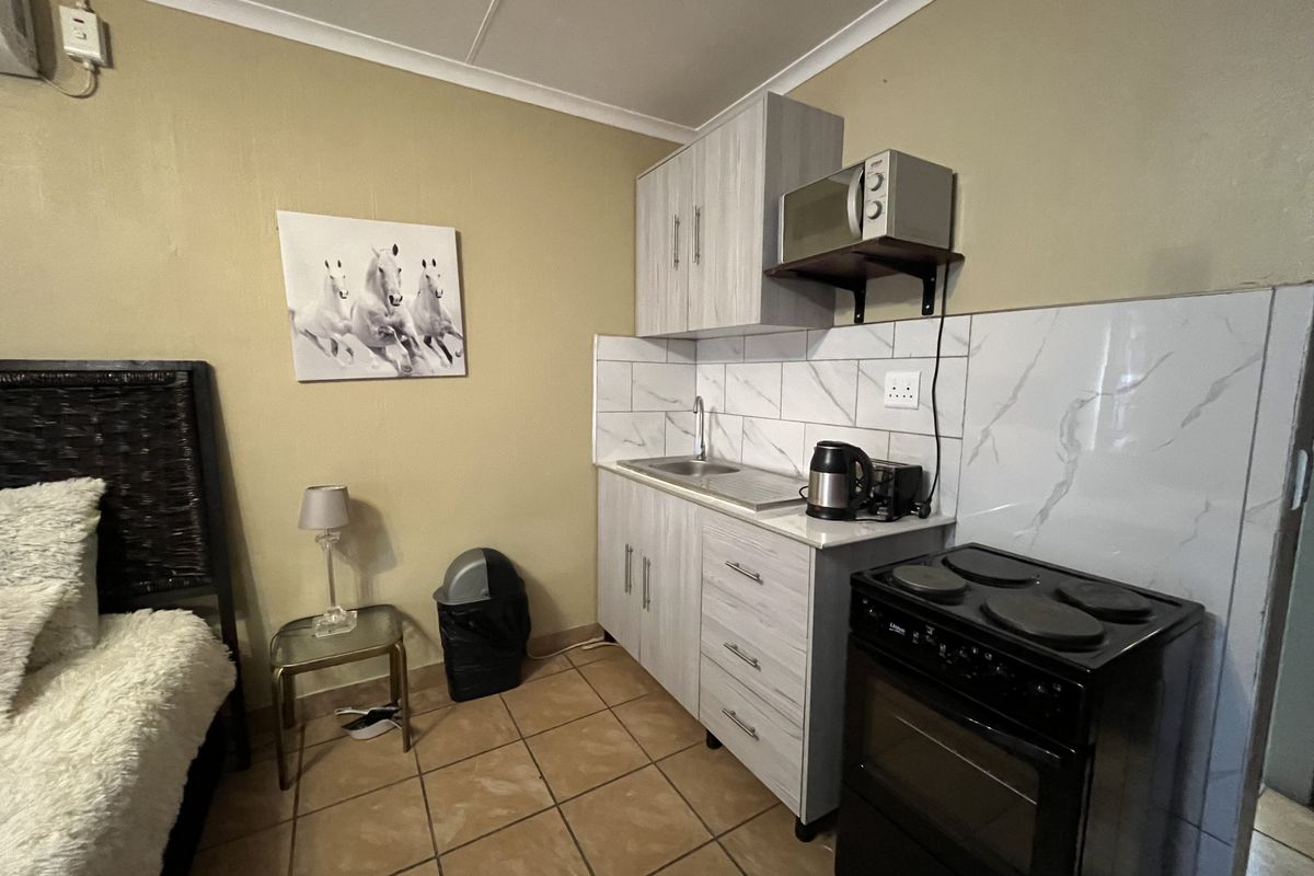 Compact kitchenette featuring light wood-finish cabinetry, marble-look tile backsplash, stainless steel sink, and a freestanding electric stove.