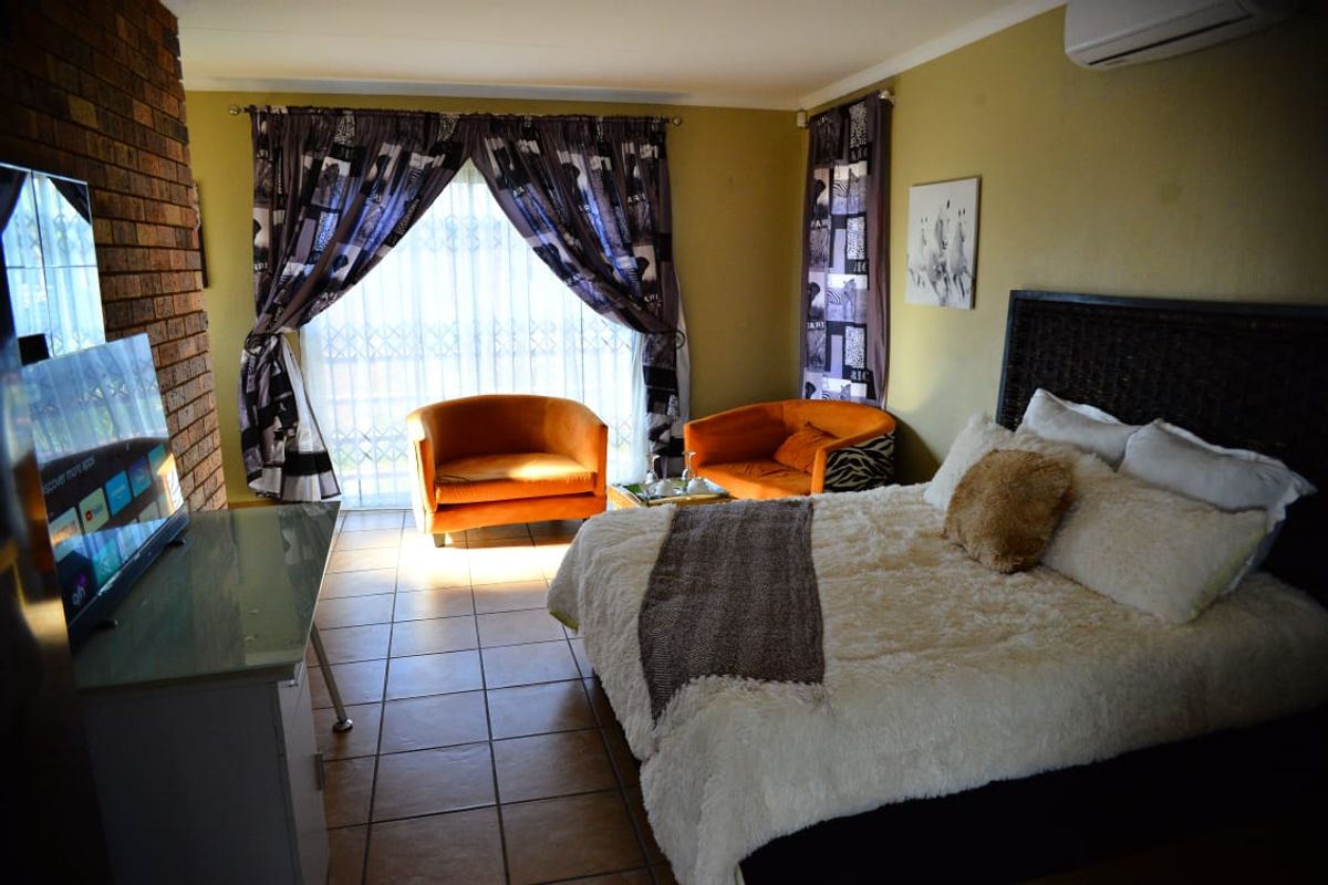 Spacious bedroom featuring an exposed brick accent wall, tiled flooring, and a wall-mounted air conditioning unit.