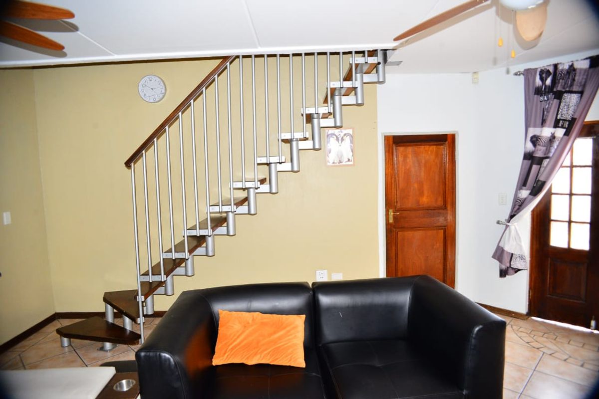 Living area featuring an open-tread staircase with metal balustrade, tiled flooring, and a ceiling fan, providing access to the upper level.