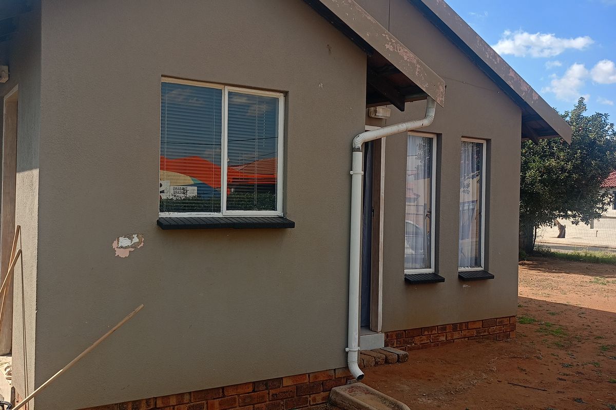 Exterior view of the house featuring a painted plaster finish, brick base, and multiple windows with external downpipe drainage.