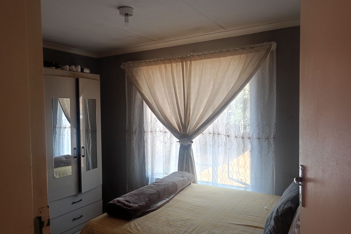 A bedroom featuring a built-in wardrobe and a window with curtains, providing a functional living space.