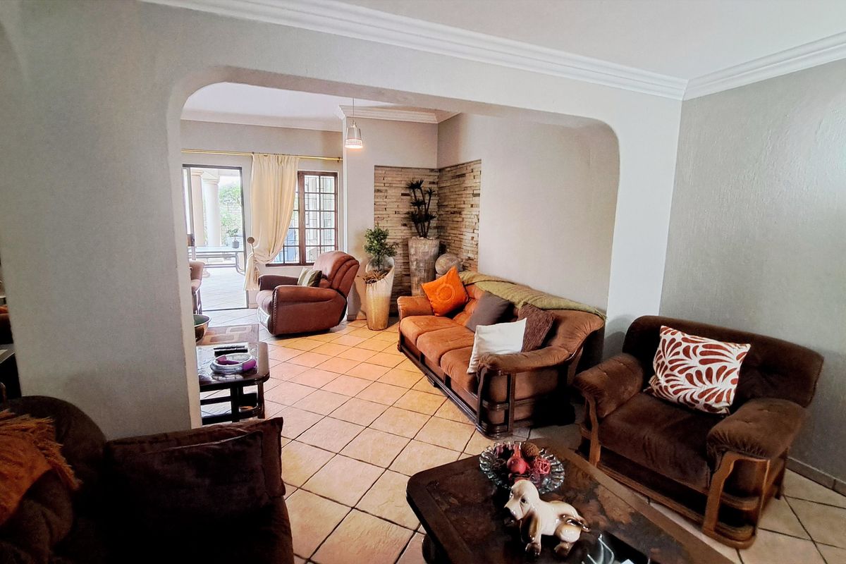 Spacious living area featuring ceramic floor tiles, a decorative stone feature wall, and an arched transition leading to an outdoor patio area.